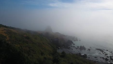 aerial: drone shot pushing towards a mysterious rock formation shrouded by fog