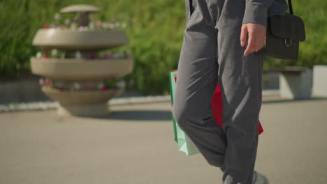 회색 조거와 캔버스 신발을 입은 사람이 초록색, 민트색, 빨간색 쇼핑 가방과 검은색 드백을 들고 는 모습, 배경은 초록색으로 약간 흐릿합니다.