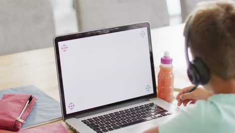 un chico caucásico feliz sentado en la mesa y usando una computadora portátil con espacio para copiar, en cámara lenta.