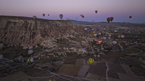 Göreme-Turkey-Aerial-v42-flyover-fields-of-colorful-hot-air-balloons-rising-up-in-the-sky-surrounded-by-rocky-ridges-of-unique-volcanic-rock-formations-at-dawn---Shot-with-Mavic-3-Cine---July-2022