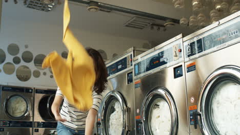 alegre caucásica joven mujer hermosa divirtiéndose y riendo como tirando ropa de la canasta en el servicio de lavandería. feliz chica satisfecha arrojando ropa en las lavadoras.