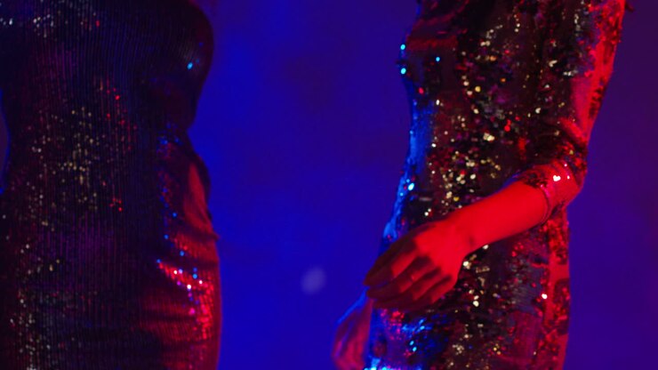 Primo piano dei busti di due donne in un locale notturno, bar o discoteca che ballano indossando abiti scintillanti