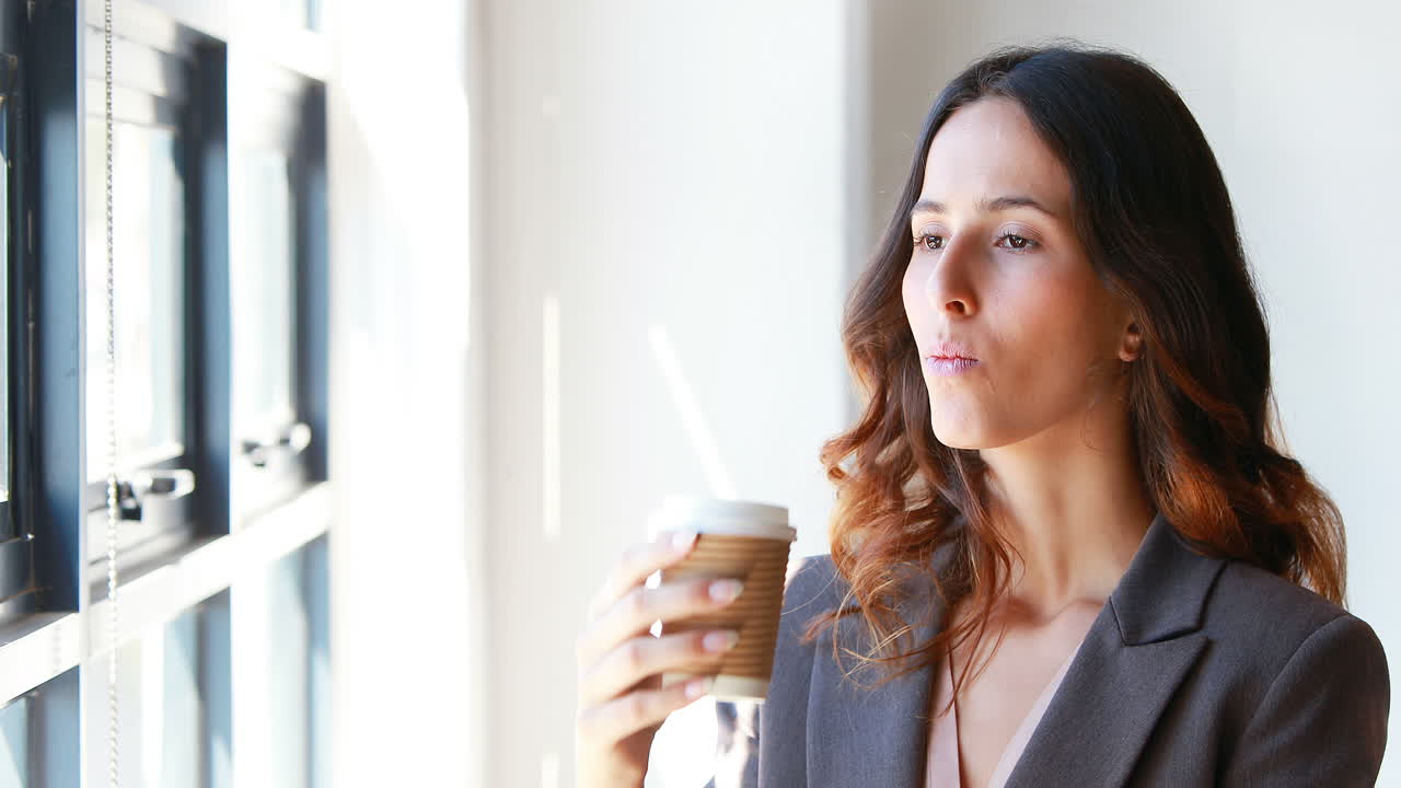 una mujer de negocios bebiendo café junto a la ventana.
