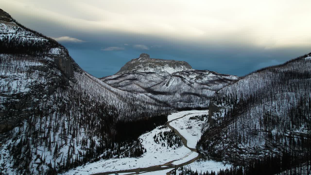 drone volando hacia atrás revelando el valle nevado en la montaña rocosa canadiense al atardecer