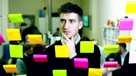 portrait of a smiling man in a thoughtful and creative agency with colorful notes and planning hanging behind the glass and the working people.