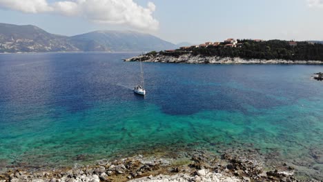 Aerial-orbit-View-Of-Sailboat-Floating-In-The-Crystal-Clear-Water-Of-Paralia-Emplisi-In-Greece