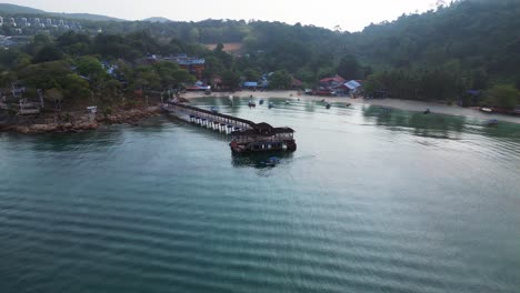 Ambiente-Matutino-Hermosa-Vista-Aérea-Rampa-De-Velocidad-De-Vuelo-De-Una-Isla-Tropical-Con-Un-Largo-Muelle-De-Madera-Que-Conduce-A-Un-Restaurante-Flotante,-Rodeado-De-Aguas-Turquesas-Y-Una-Exuberante-Selva-Tropical