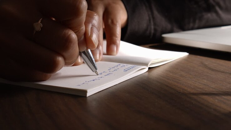 Una giovane donna che scrive nel suo quaderno con una penna nel suo appartamento mentre lavora da casa