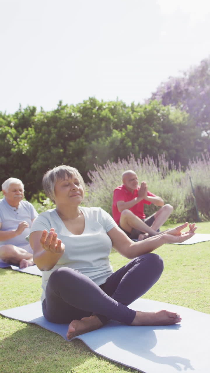 Vertical video of happy senior biracial woman doing meditation with friends in garden, slow motion