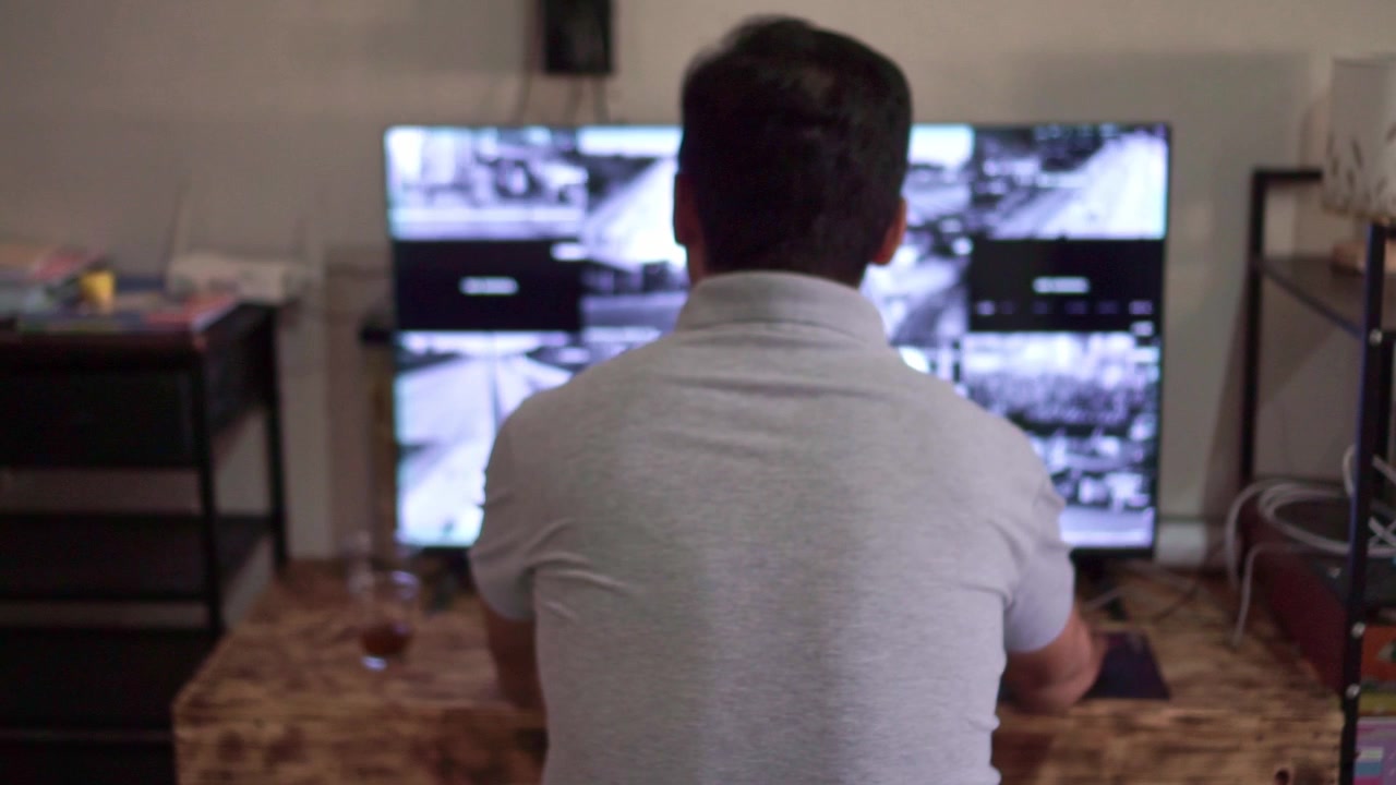 Guardia di sicurezza da dietro che esamina i filmati delle telecamere a circuito chiuso su due monitor, configurazione della stanza buia, monitoraggio della sorveglianza e concetto di flusso di lavoro per l'osservazione della sicurezza.