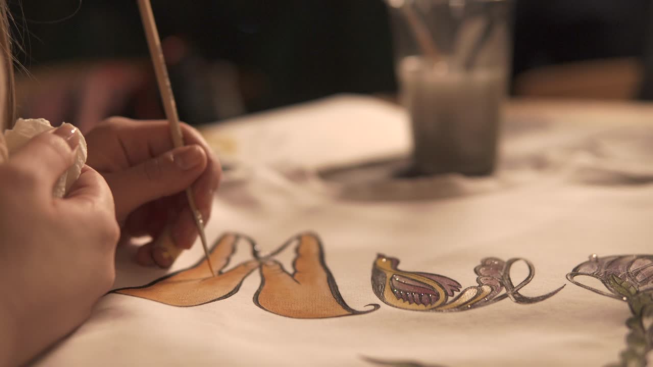 Close-up of female hand with paintbrush is painting white shirt in a workshop