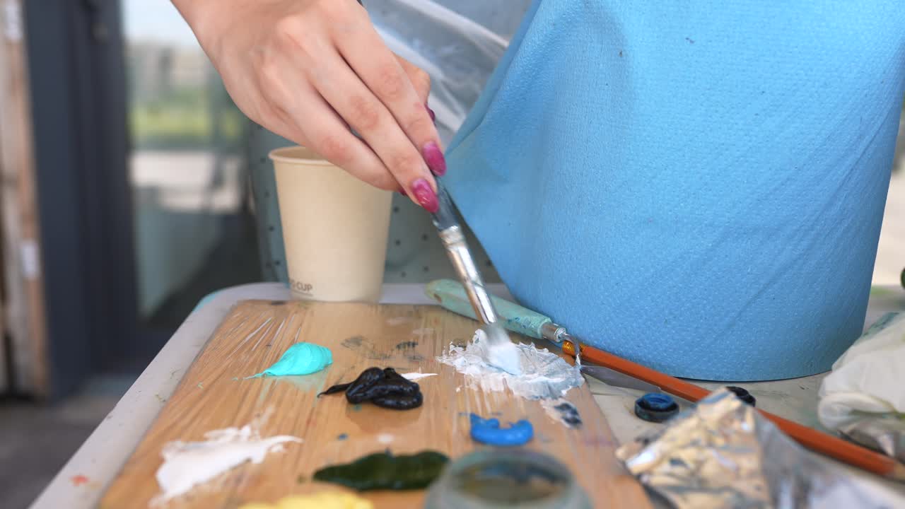 mujer pintando con pincel en una paleta de madera