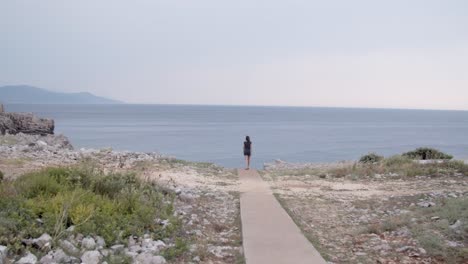 chica caminando por el sendero de la playa y mirando hacia el acantilado del mar, tiro ancho