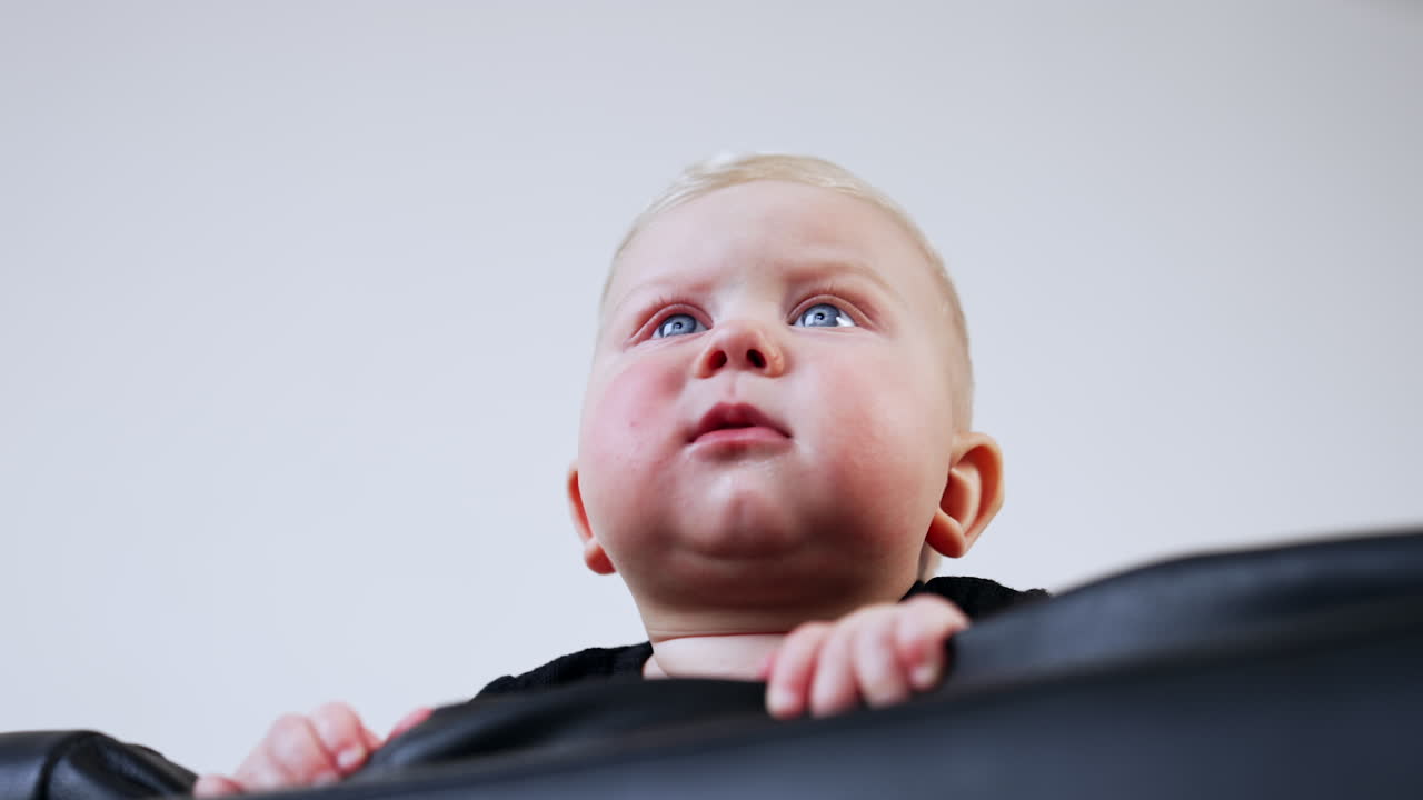 Adorable cute child with plump cheeks on the leather sofa. Low angle view on the lovely child smiling.