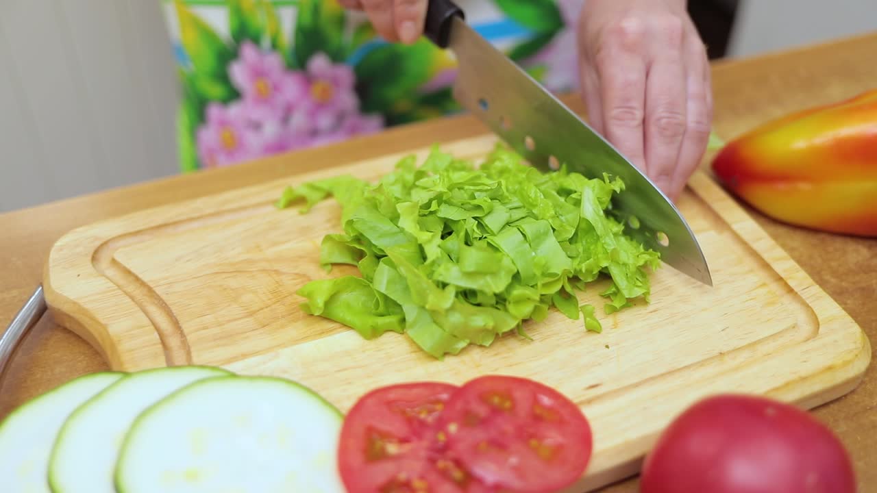 manos femeninas de la ama de casa con un cuchillo cortado lechuga fresca en una mesa de cocina de corte de tabla