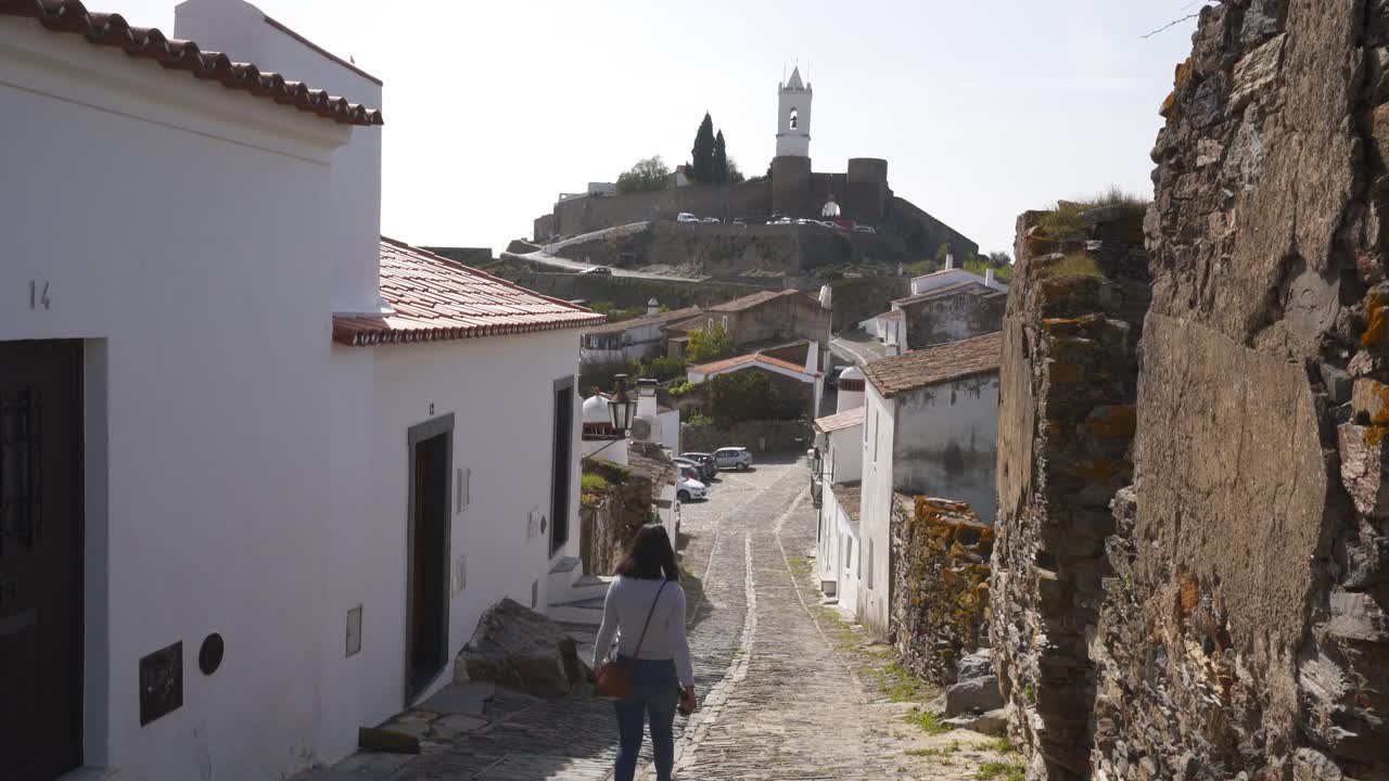 Donna che cammina per la strada del villaggio di Monsaraz con case bianche in Alentejo, Portogallo