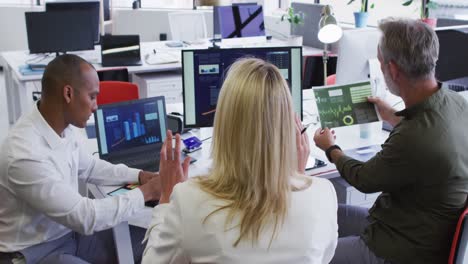 Diverse-business-people-sitting-using-computer-and-takling-at-desk-in-office