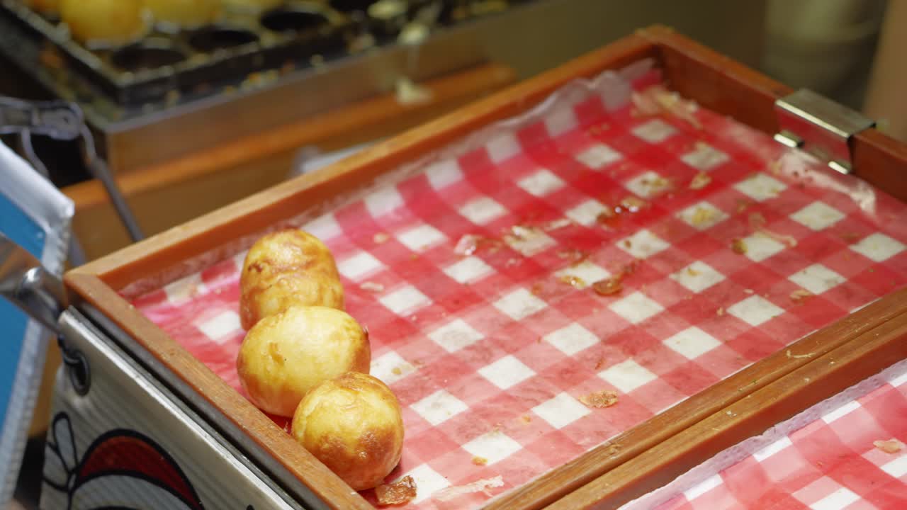 Un venditore di street food raccoglie polpette takoyaki appena cucinate, preparandole per servirle in una bancarella affollata.