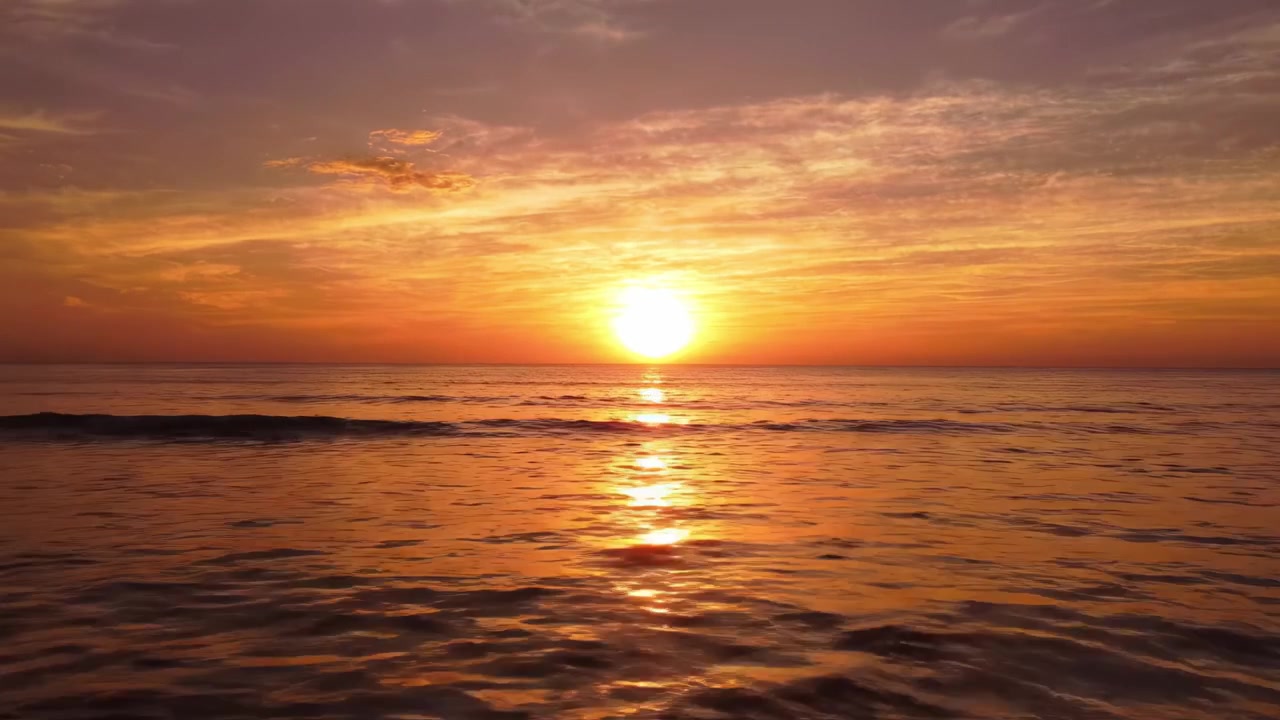 En betagende solnedgang over det rolige hav, hvor solen dykker ned under horisonten og oplyser himlen med levende nuancer af orange og guld, hvilket skaber en fredfyldt atmosfære.