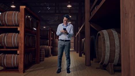 full body of an asian male professional worker standing with his smartphone in cellar of winery, working continuously
