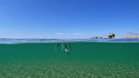 unusual half underwater view of lost diving mask with snorkel floating on sea water surface with trabocchi fishing wooden platforms in background