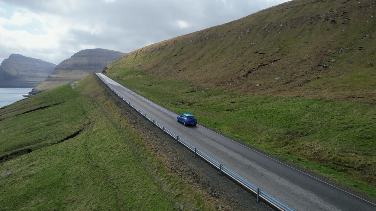 Aerial view of a vehicle traveling along a scenic highway through a green valley in the Faroe Islands