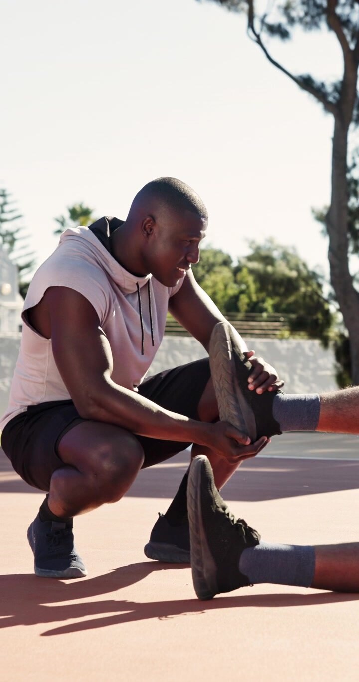 Personal Trainer Assisting Athlete with Leg Stretch on Outdoor Court