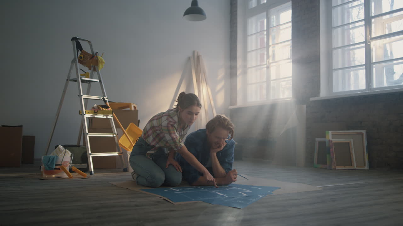 Par diskuterer oppussing innendørs. Familie studerer plantegninger på gulvet.