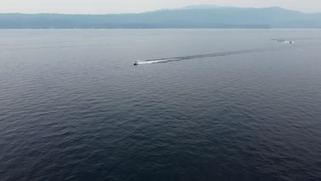 Drone-shot-of-a-jet-ski-driving-from-right-to-left-screen-at-Payette-Lake-in-McCall,-Idaho-with-the-mountains-in-the-background