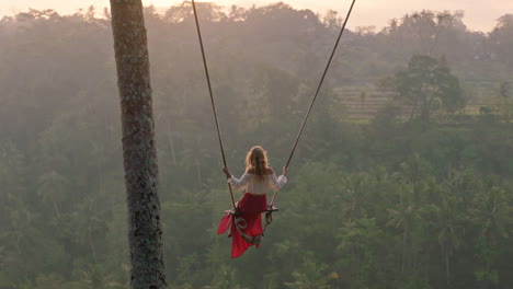 travel woman swinging over tropical rainforest at sunrise female tourist sitting on swing with scenic view enjoying freedom on vacation having fun holiday lifestyle slow motion