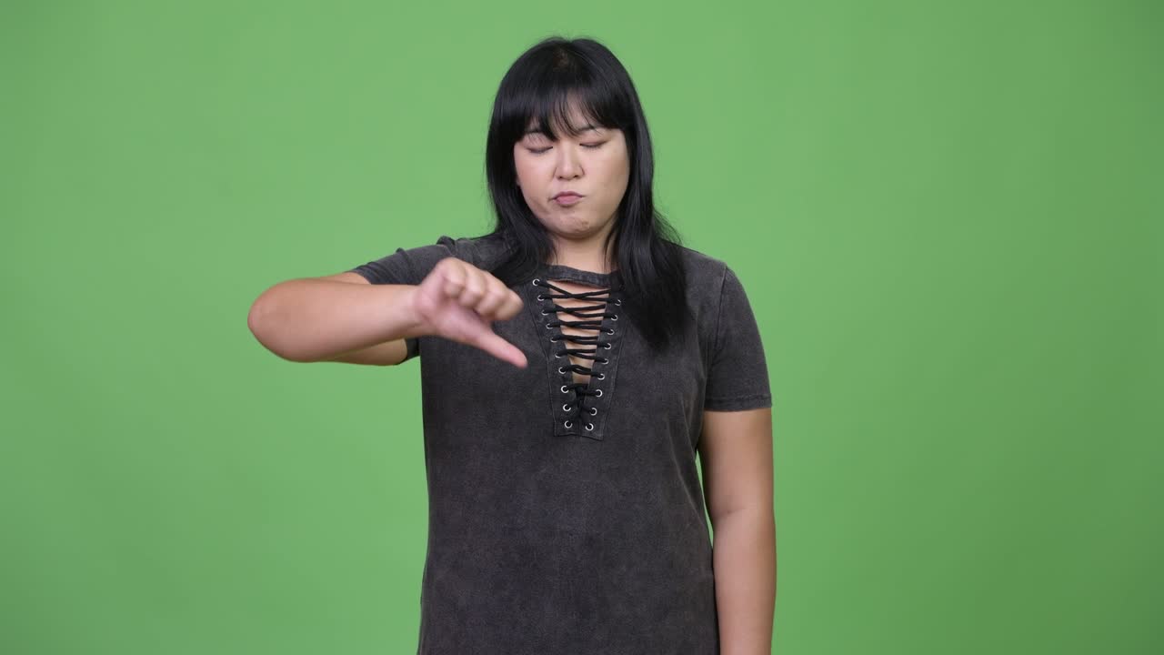 Sad overweight Asian woman giving thumbs down