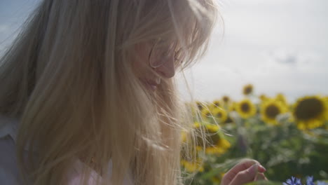 blonde woman smells purple flowers by sunflower field, side close-up