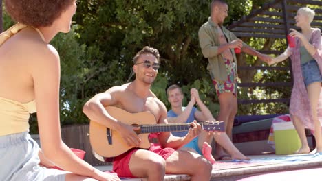 happy diverse group of friends with drinks playing guitar at pool party in summer