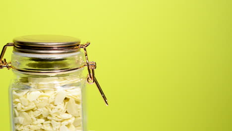 Detalle-De-Un-Tarro-De-Albañil-Hermético-Que-Gira-Con-Almendras-En-Rodajas-Sobre-Un-Fondo-Amarillo-Neón