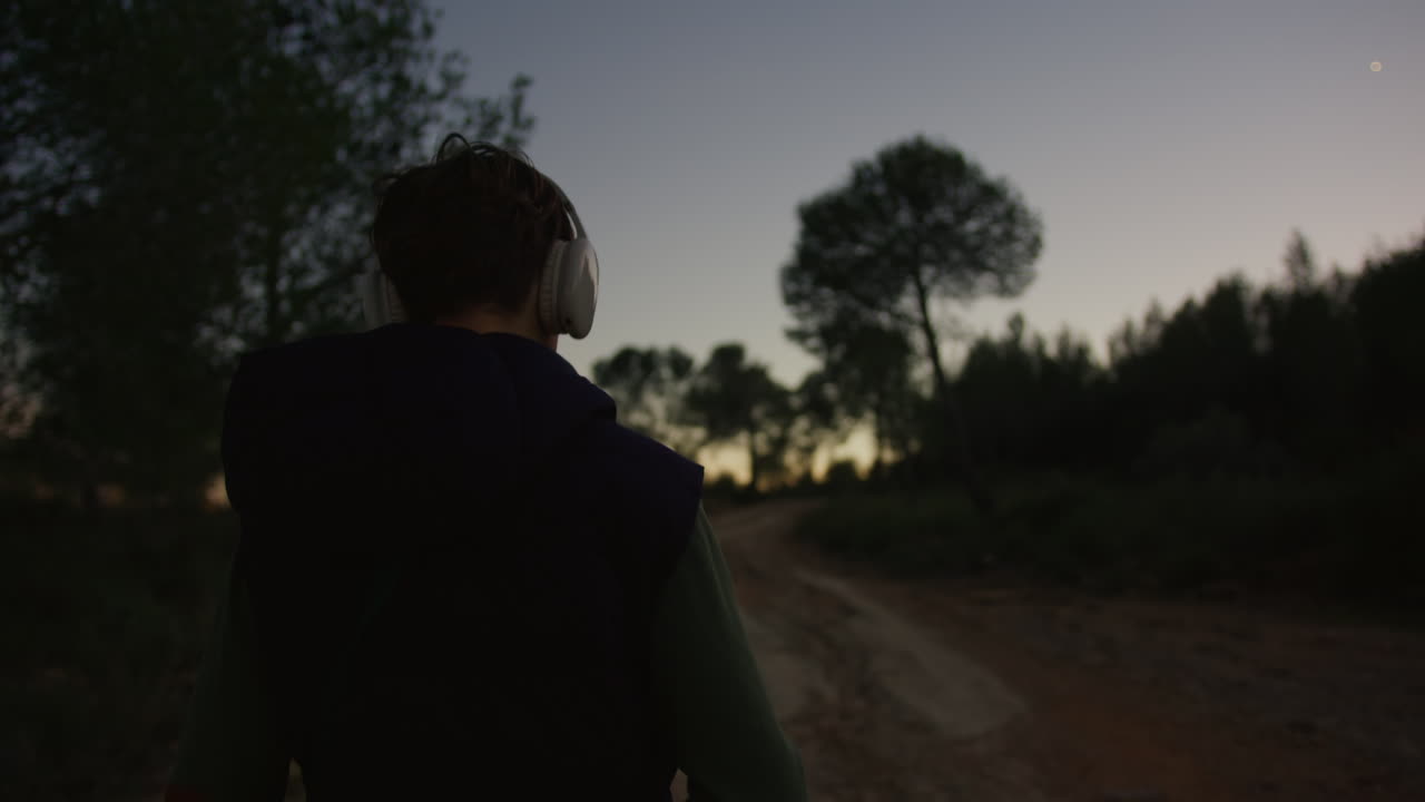 Persona che cammina in un bosco al crepuscolo, ascoltando musica con le cuffie