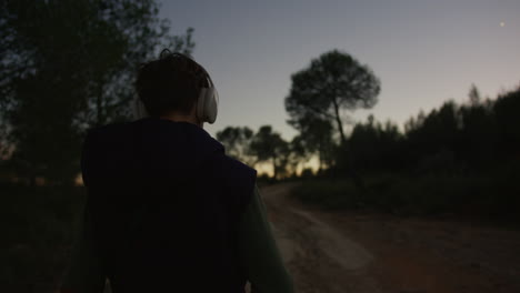 persona caminando en un bosque al crepúsculo, escuchando música con auriculares