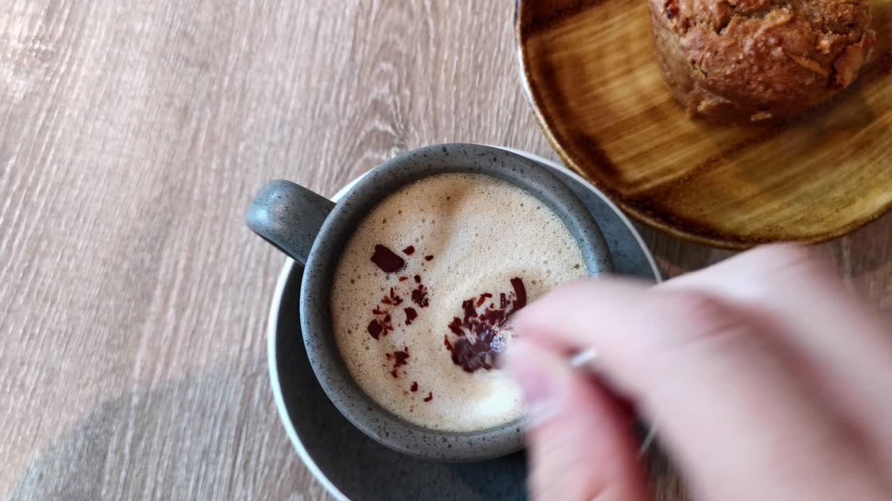 카페에서 카푸치노와 머핀을 먹고 작은 티스푼으로 커피를 손으로 젓는 모습