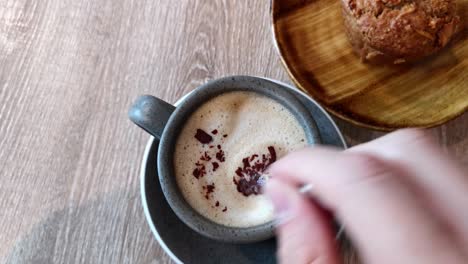 pov of having a cappuccino and a muffin in a café, hand stirring the coffee with small teaspoon