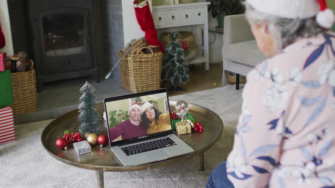 mujer caucásica mayor usando una computadora portátil para una videollamada de navidad con una pareja sonriente en la pantalla