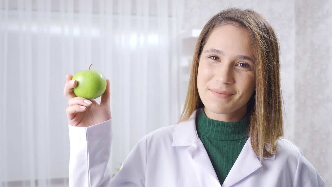 una dietista positiva recomienda una alimentación saludable, muestra manzanas frescas.