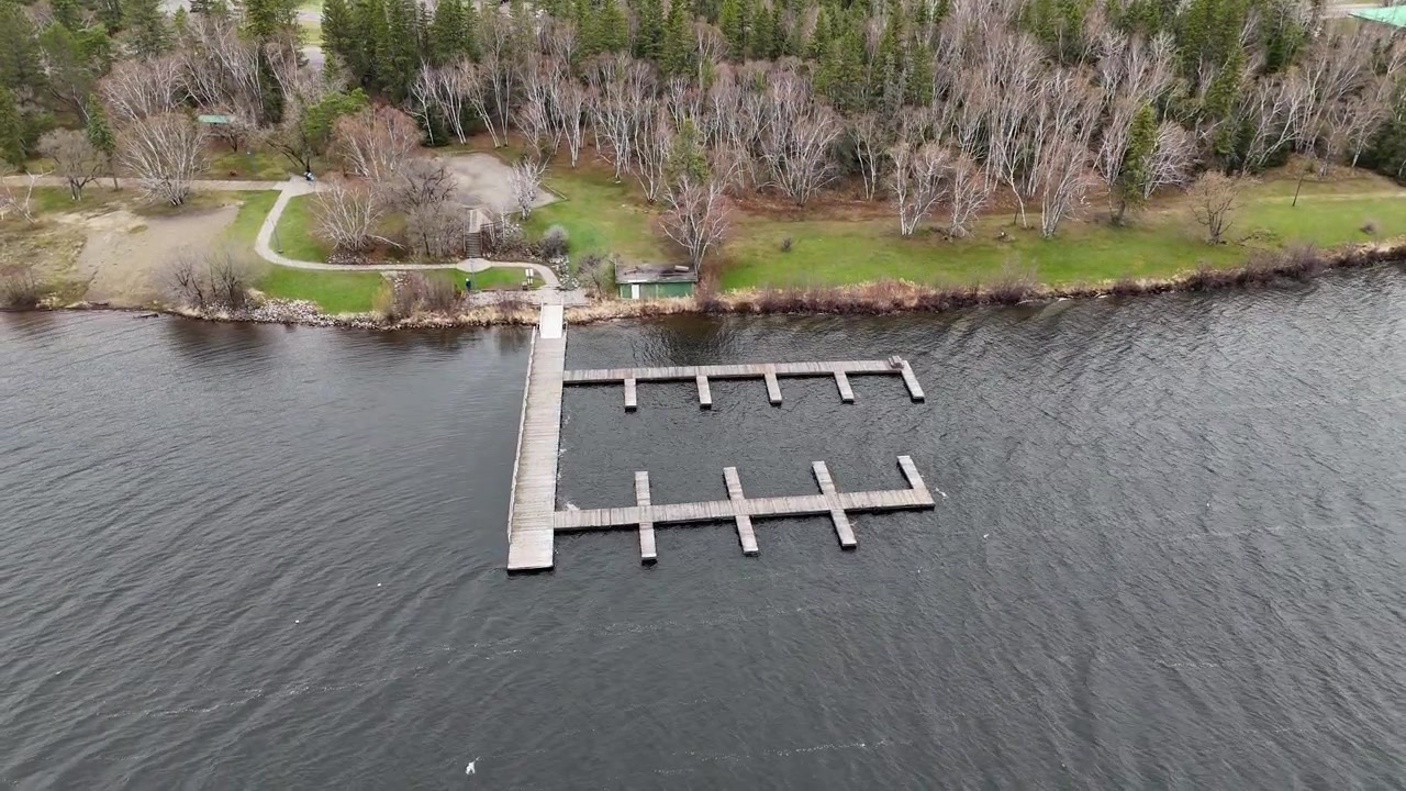 Bådebro ved Falcon Lake i Whiteshell Provincial Park, Manitoba. Drone kigger mod tomme bådpladser, mens den stiger op og afslører søvand, træer langs kystlinjen og forårsforhold på en overskyet dag
