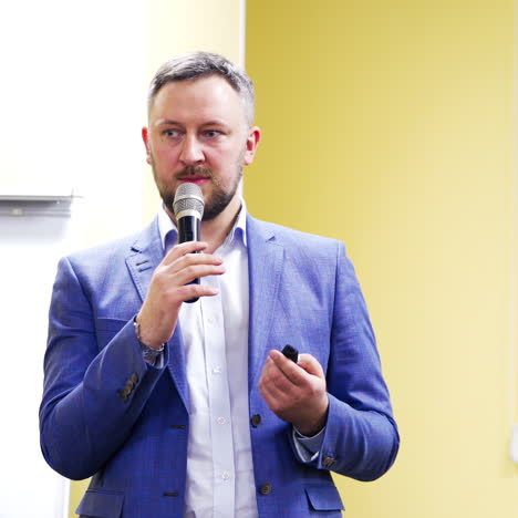 businessman in suit with microphone gives the lecture indoors. handsome speaker conducts speech on the business forum. professional ideas, politics or economy.