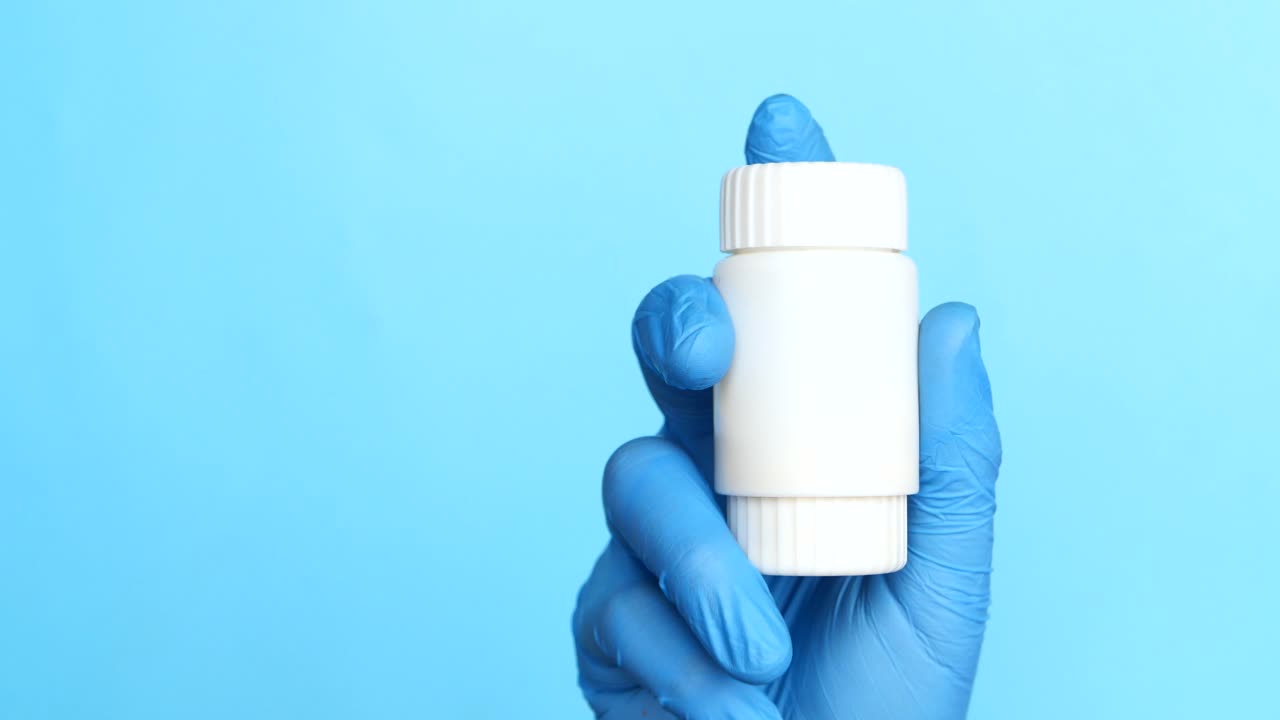 Mano con guanti blu che tiene un flacone di pillole bianco