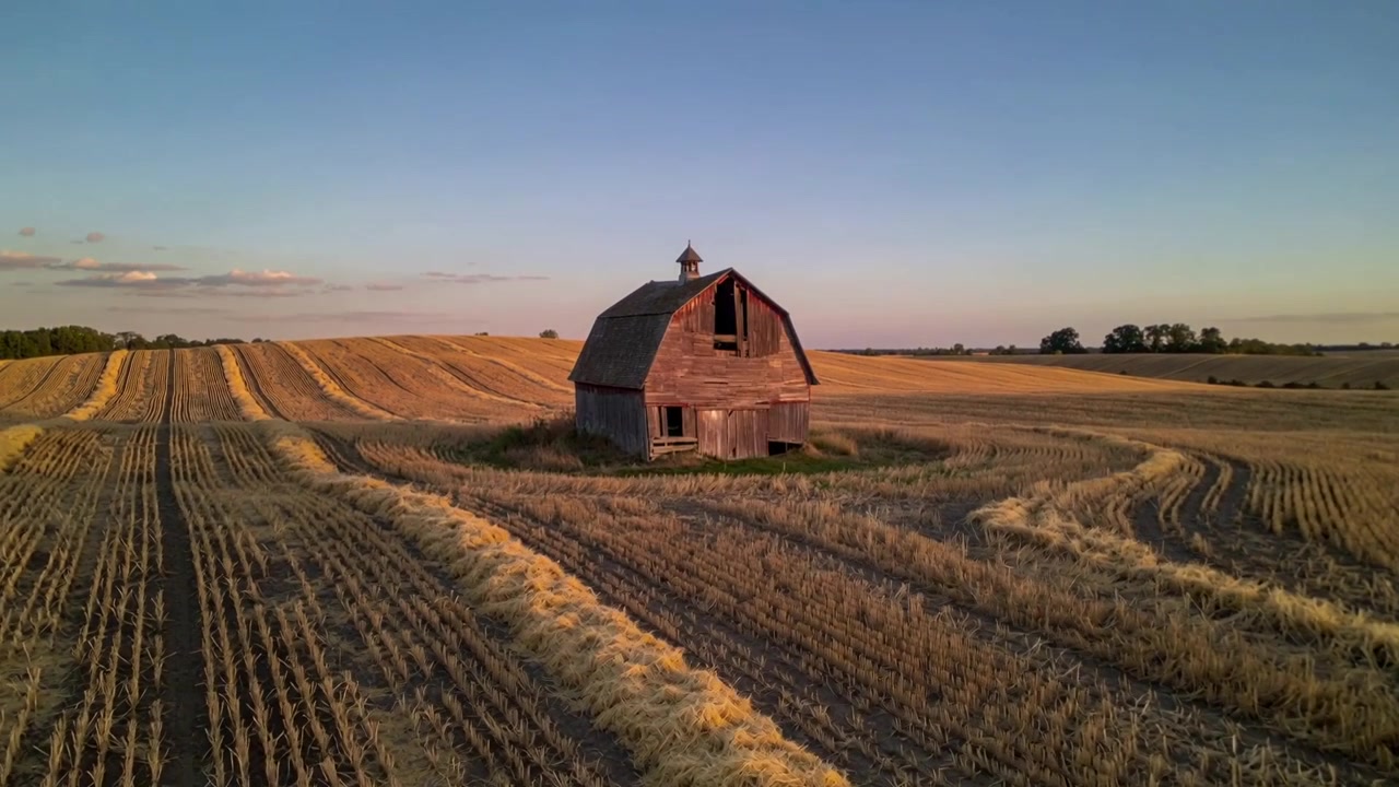 Faldende drone starter fra et bredt luftfoto, nærmer sig en trælade med mansardtag og afslører klippede rækker.