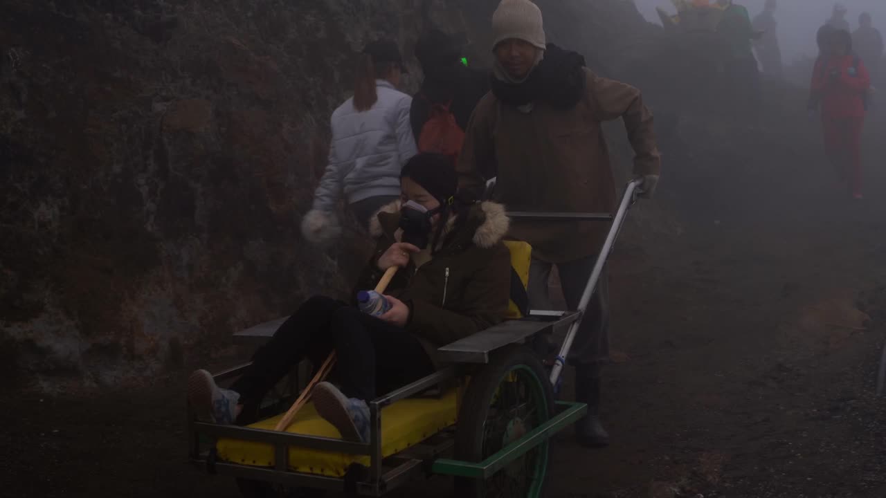 A Javanese man pushes a Chinese Tourist wearing a gas mask on down a rocky pathway at the volcano Mount Ijen in East Java Indonesia