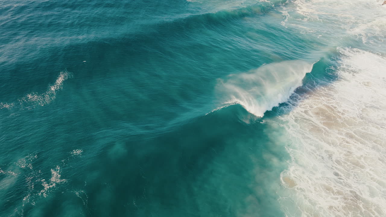 Clean turquoise wave breaking near rocky shoreline with textured ocean surface