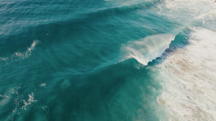 Clean turquoise wave breaking near rocky shoreline with textured ocean surface