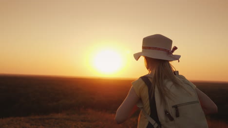 chica divertida con un sombrero de paja corre colina abajo al atardecer sostiene el sombrero con las manos leto y la aspiradora