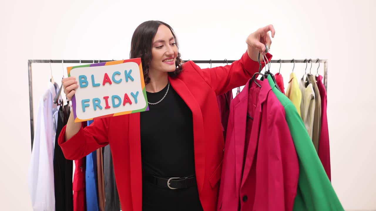 Woman holding 'Black Friday' sign and clothes, excited about sales