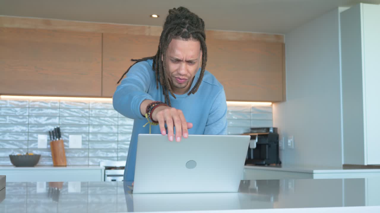 Uomo afroamericano che entra in cucina e risolve un problema sul bancone dell'isola con un laptop.